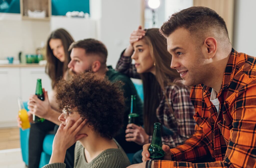 group of friends drinking while watching tv at home, concept of teen drinking habits
