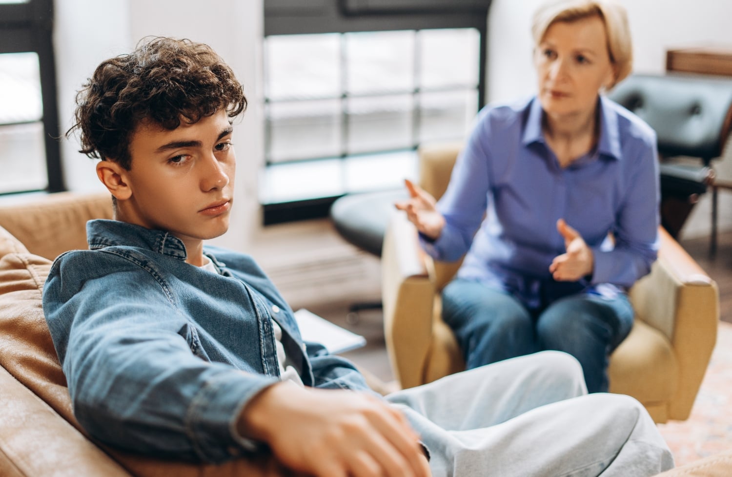Professional psychologist talking with depressed teenage boy feeling guilty about behavior during therapy at office. Psychological support concept.