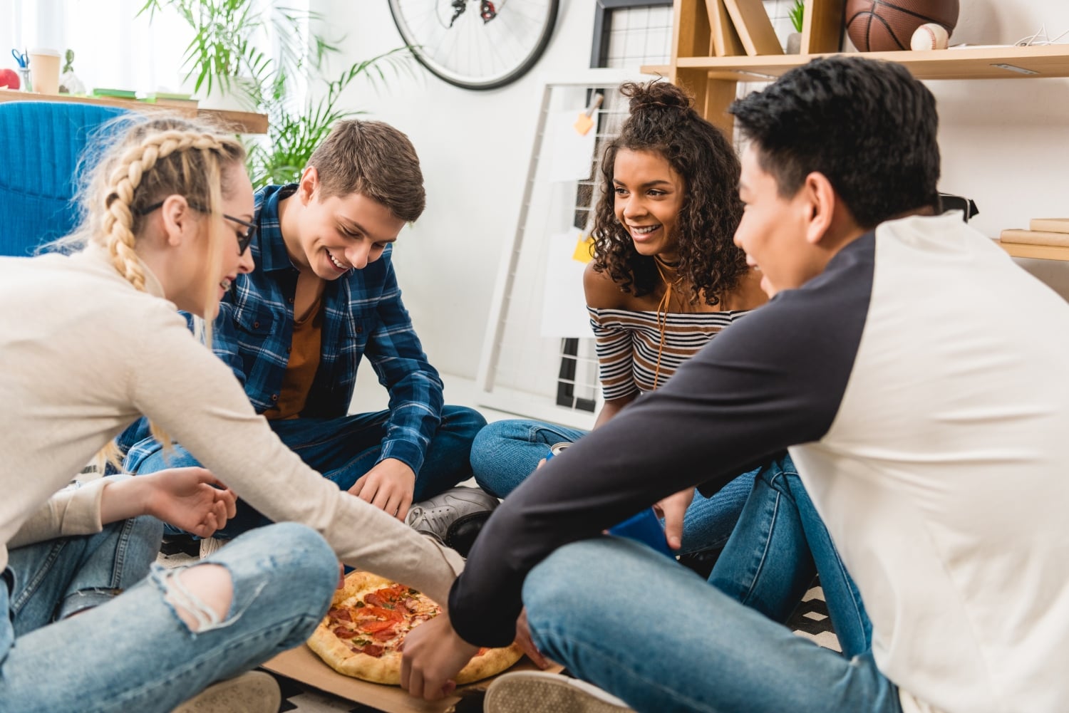 multiethnic teen friends sitting on floor and eating pizza
