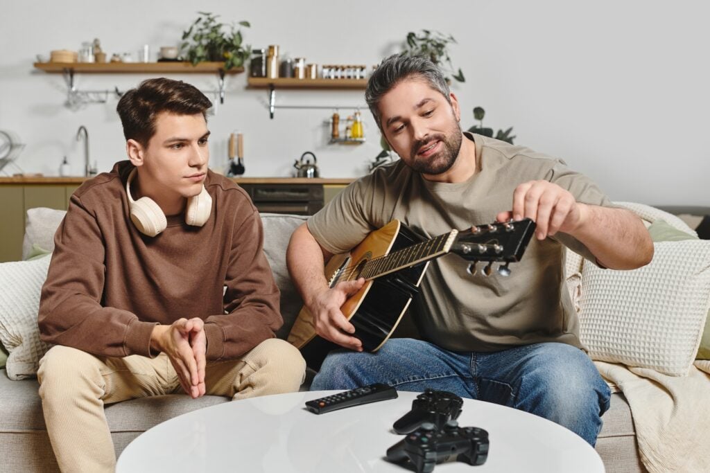 dad teaching teenage son to play the guitar