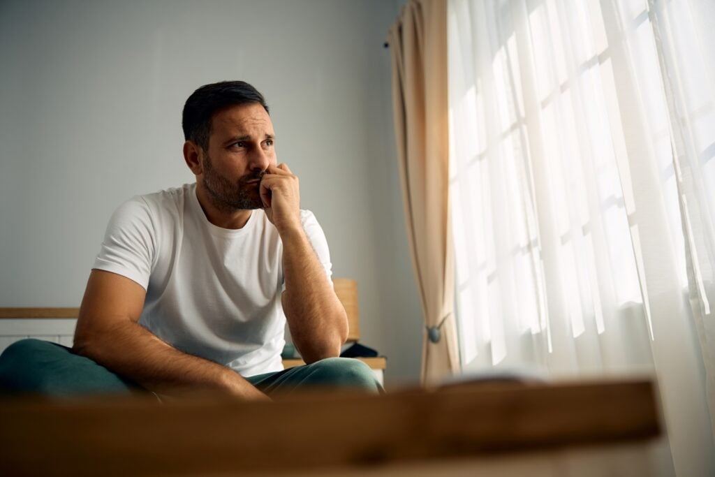 man looking pensively toward a bright window, concept of mental health, thoughtful reflection